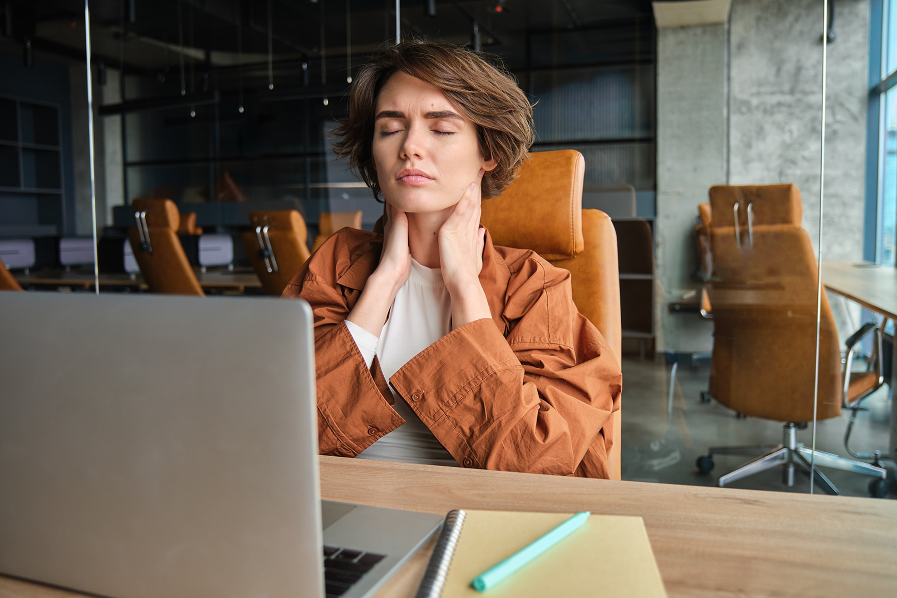 A woman holding her painful neck while working on a laptop.