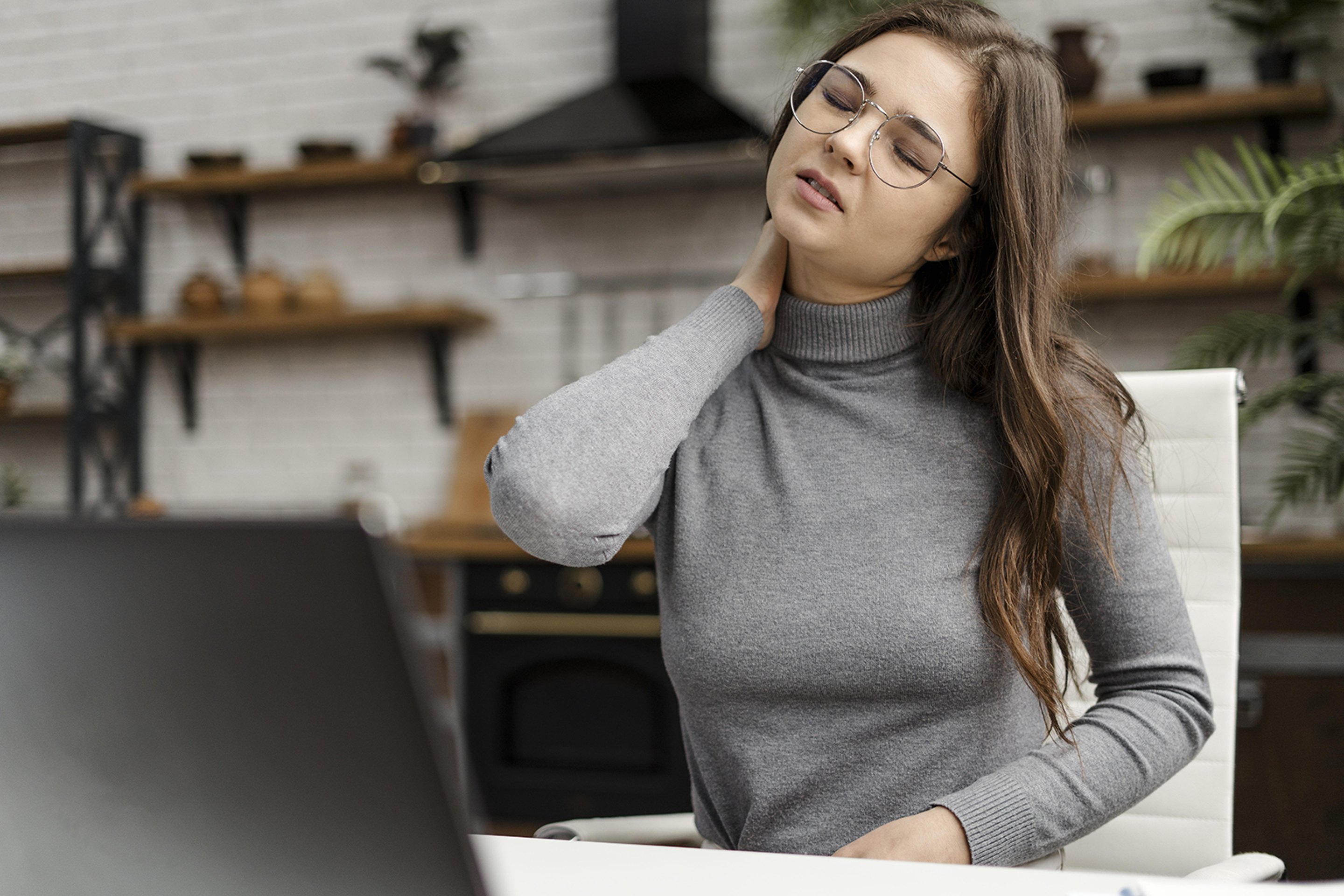 A woman rubs her neck, looking uncomfortable with pain.