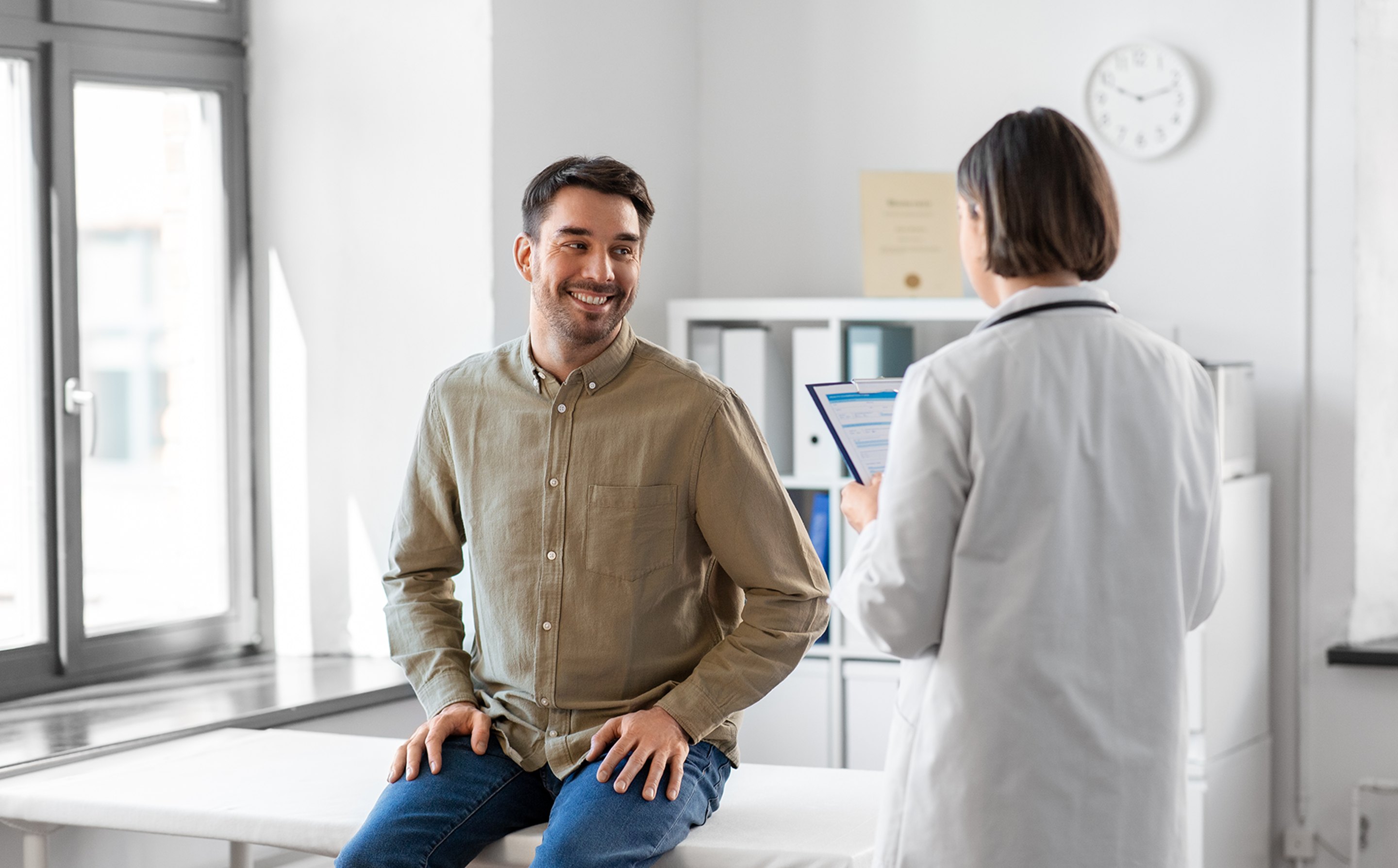 A male patient talking to a doctor about sexual health in an examination room.