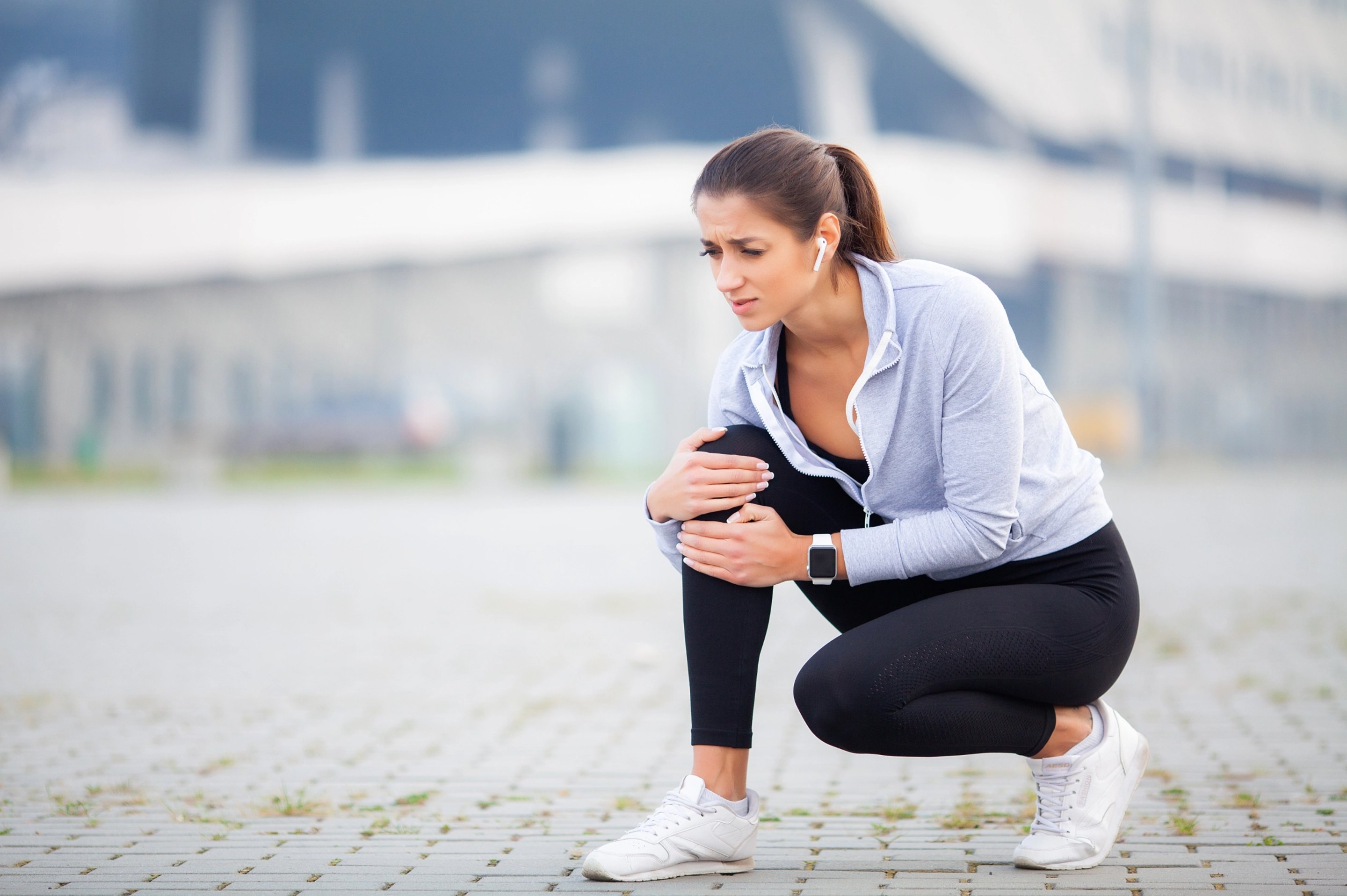 A young woman in workout clothes with joint pain, holding her knee.