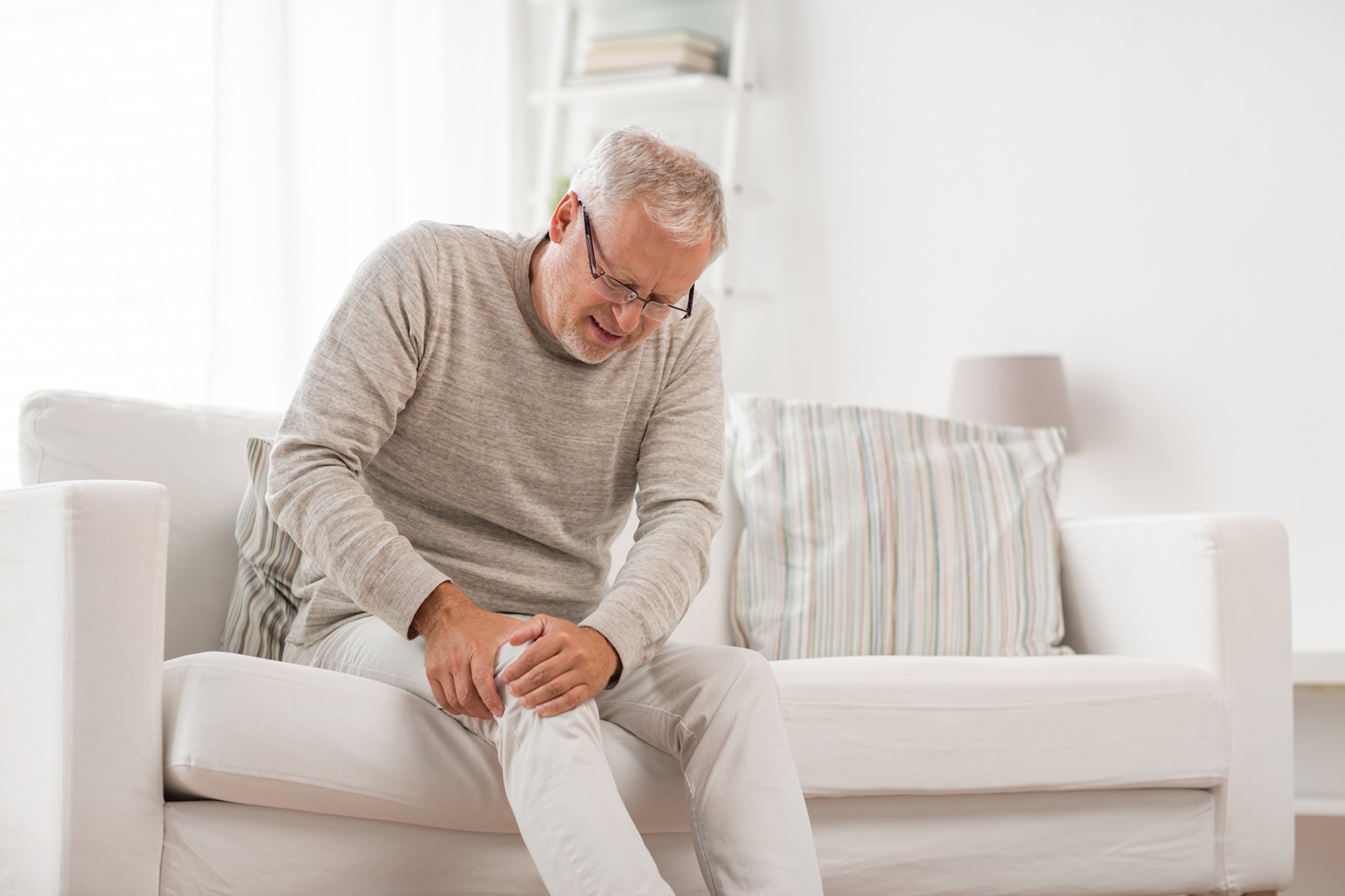 A senior man with knee pain sitting on a sofa.