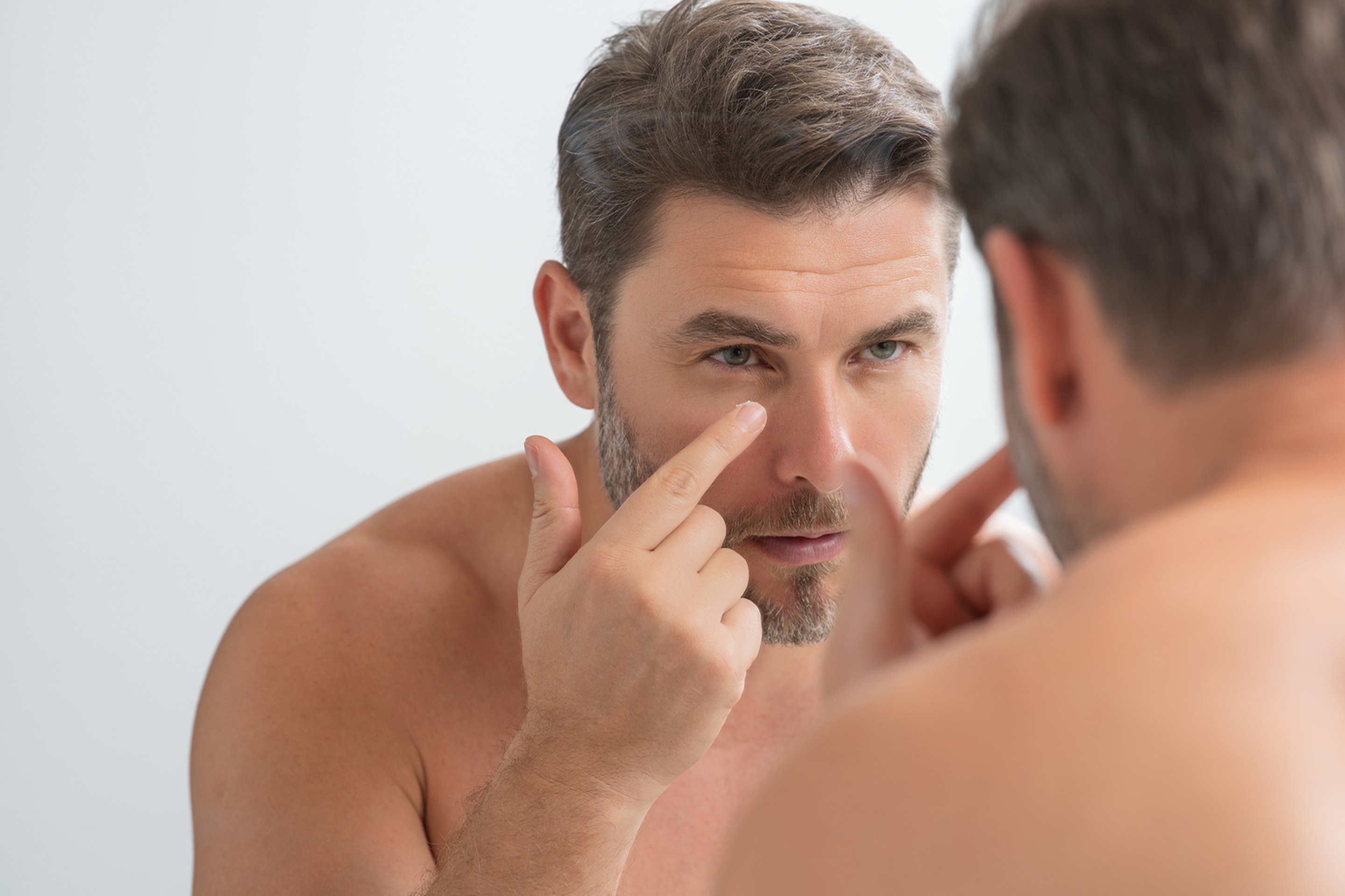 A middle-aged man examining his eyes and wrinkles for skin aging treatment.