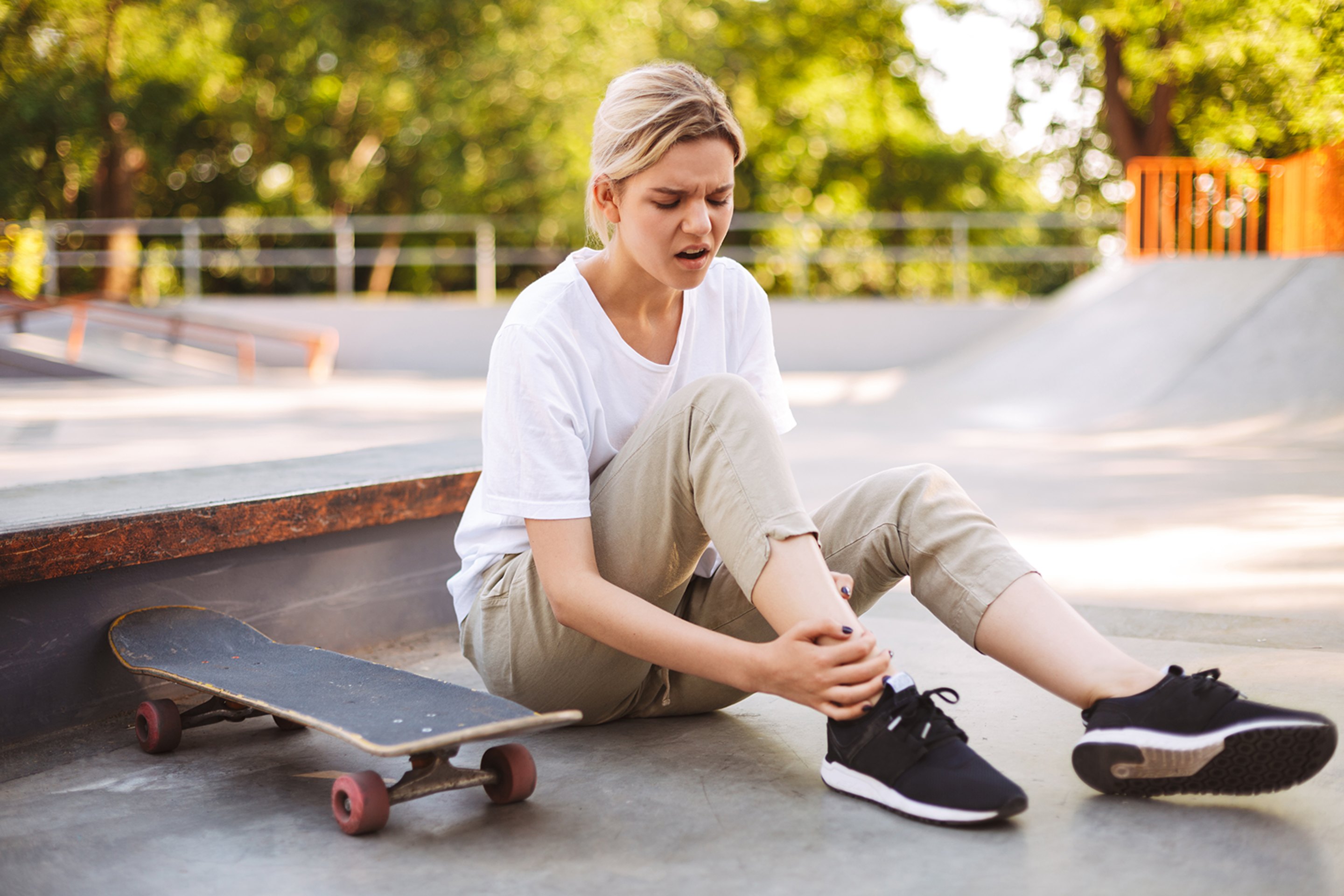 A woman sitting on the ground with her hands on a painful ankle.