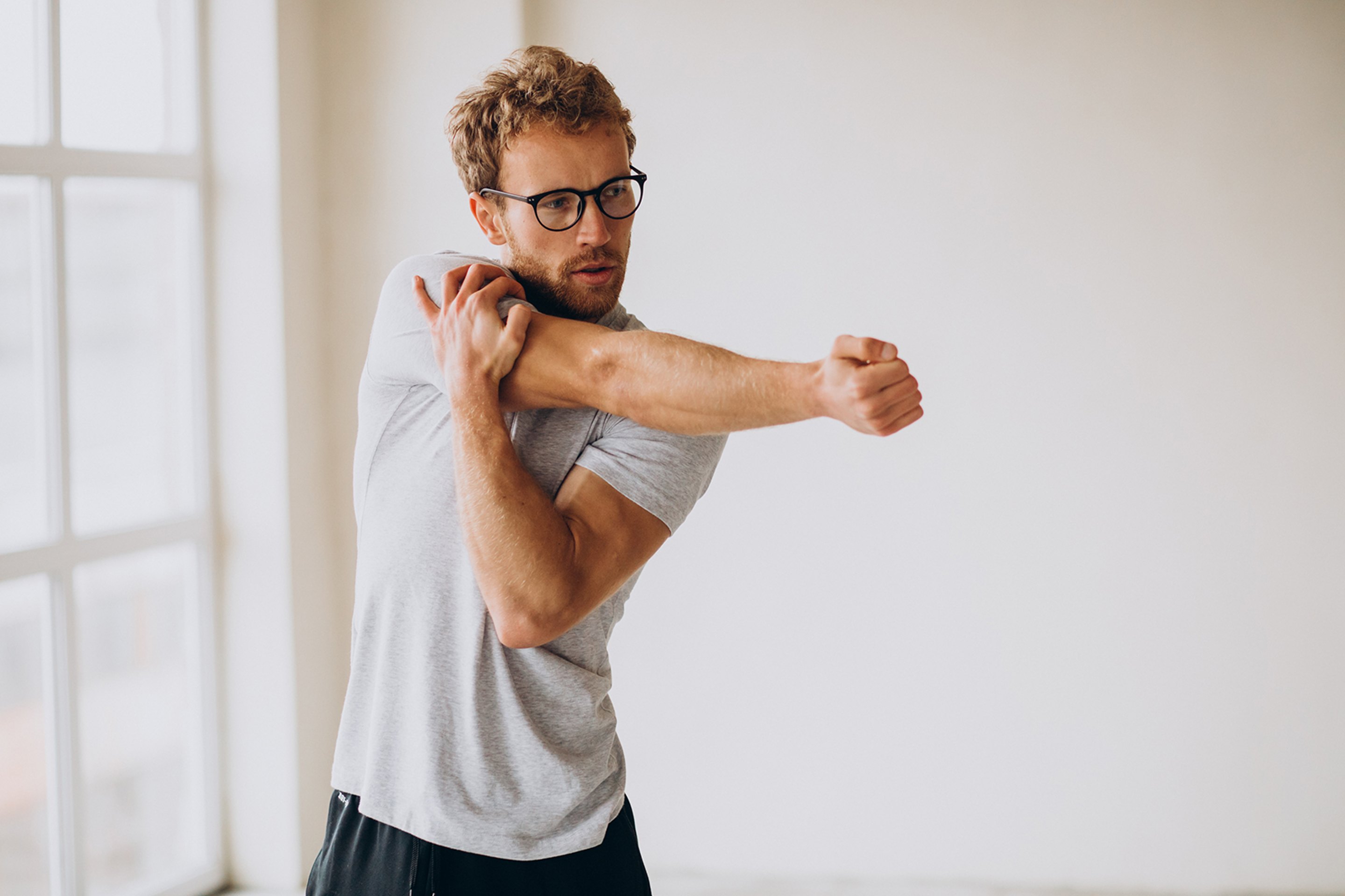 A Chiropractic patient stretching his shoulder in a gym.