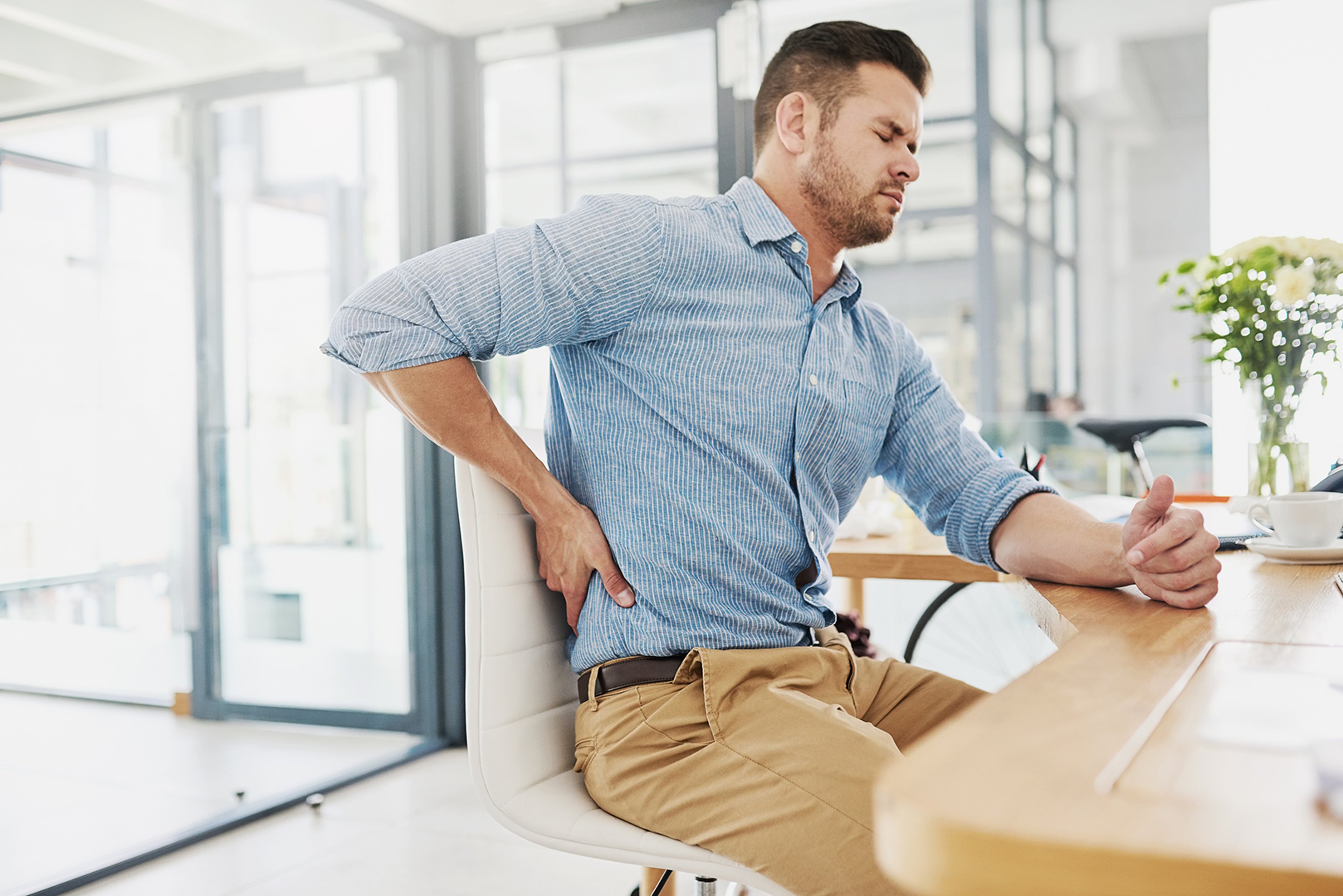 A man sitting at a table holding his painful lower back.