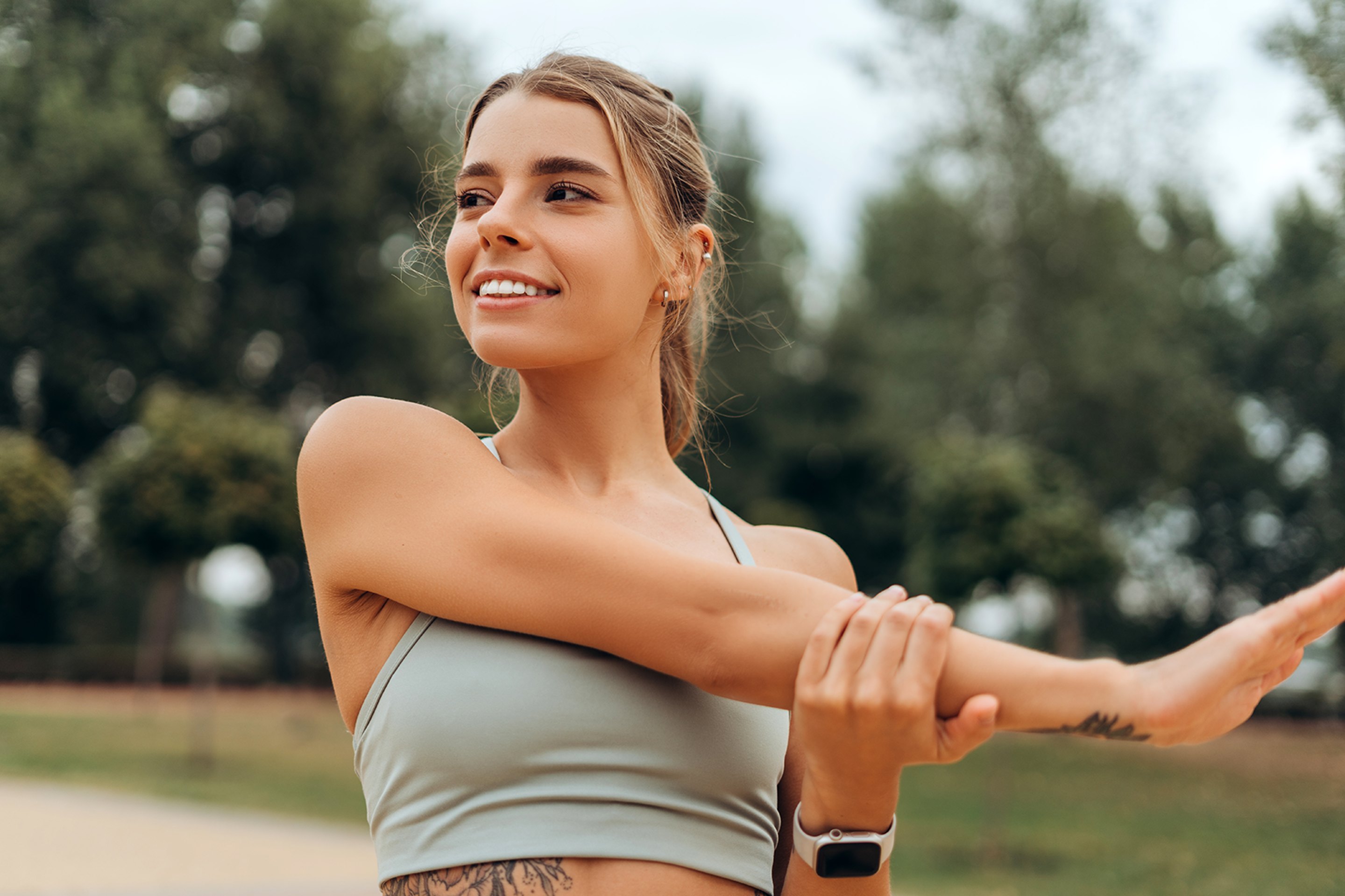 A smiling, athletic young woman stretching her arm after hormone replacement therapy.