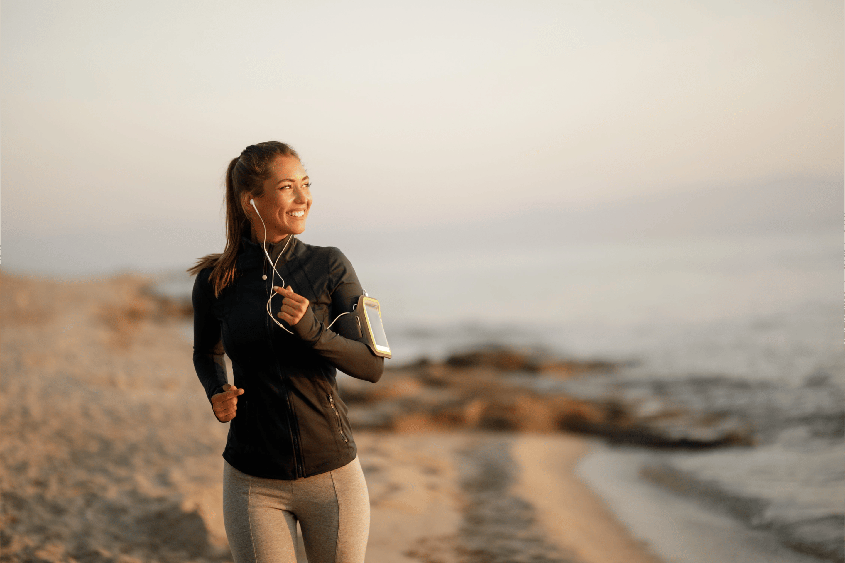 A smiling woman running on the beach with earbuds.